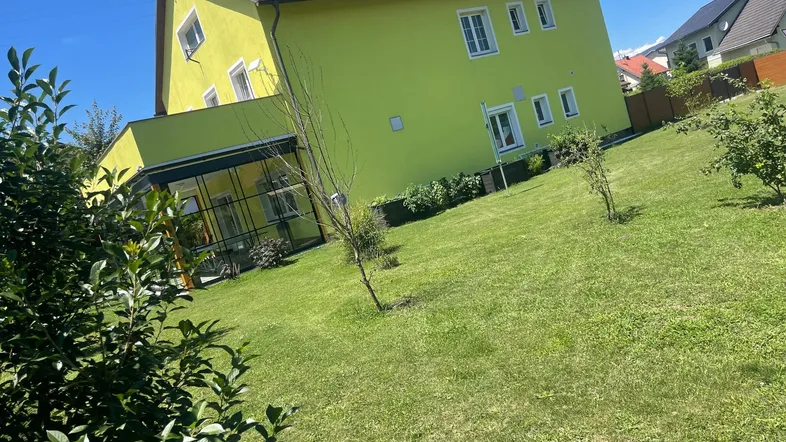 Das moderne Haus mit leuchtend gelber Fassade und großem Garten unter blauem Himmel.
