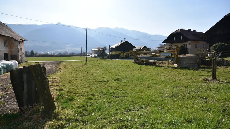 Weitläufige ländliche Umgebung mit grünen Feldern, Häusern und schneebedeckten Bergen im Hintergrund.