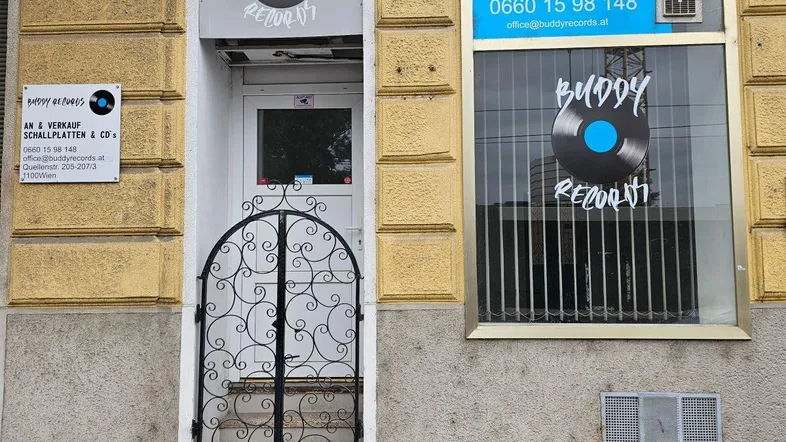 Fassade eines Gebäudes mit einem Plattenladen im Erdgeschoss und dekorativem Eisengitter vor dem Eingang.
