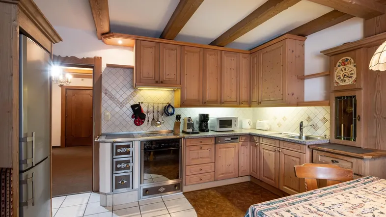 Traditionelle Holzküche mit Einbaugeräten, Fliesenboden und sichtbaren Deckenbalken, die eine gemütliche Atmosphäre schafft.