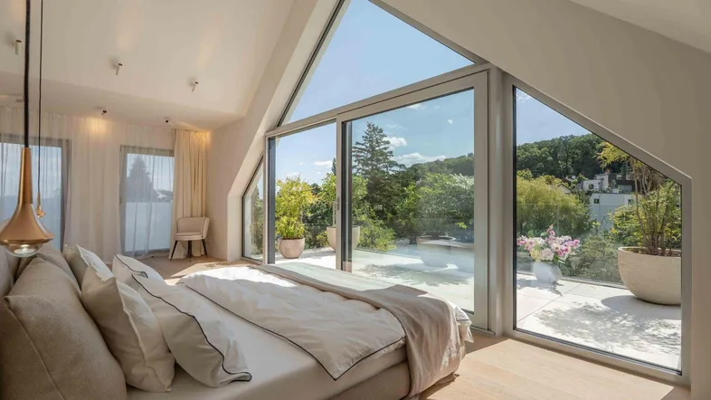 Helles Schlafzimmer im Dachgeschoss mit großen Fenstern, Dachschräge und Zugang zur Terrasse.