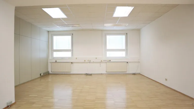 Heller, leerer Büroraum mit Laminatboden, zwei Fenstern und einer abgehängten Decke, bereit zur individuellen Gestaltung.