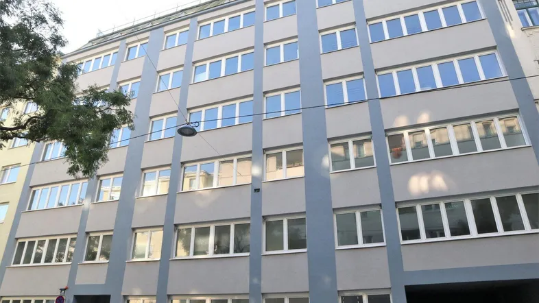 Graues Mehrfamilienhaus mit vielen Fenstern und moderner Architektur in städtischer Umgebung, gut gepflegt.
