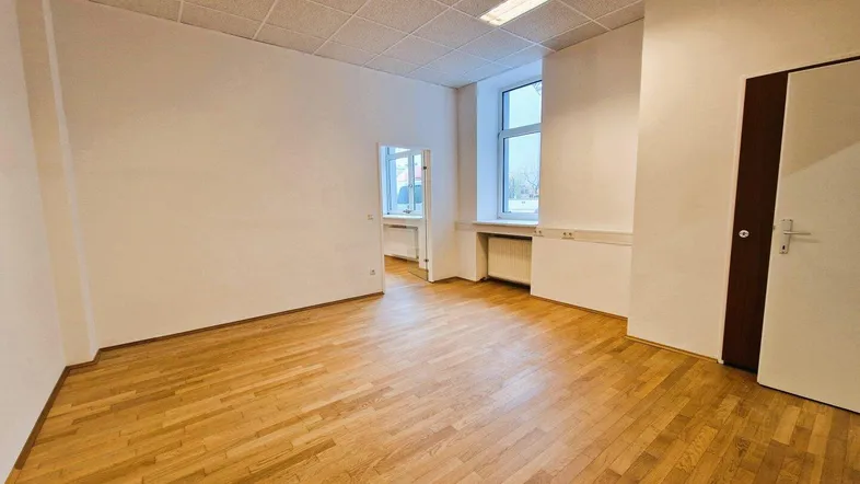 Leerer Büroraum mit Holzparkettboden, weißen Wänden und Deckenbeleuchtung, bereit zur individuellen Gestaltung.