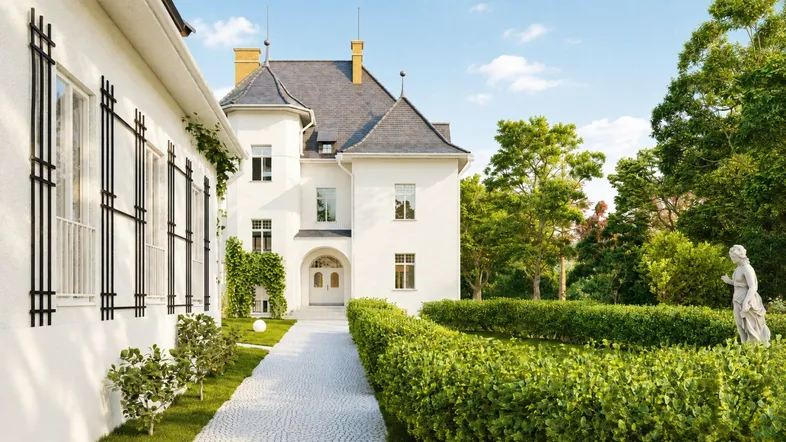 Elegante weiße Villa mit gepflegtem Garten und klassischer Architektur unter blauem Himmel.