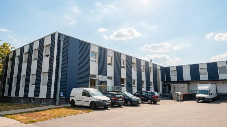 Modernes Geschäftsgebäude mit markanter blau-weißer Streifenfassade, umgeben von Parkplätzen unter einem klaren Himmel.