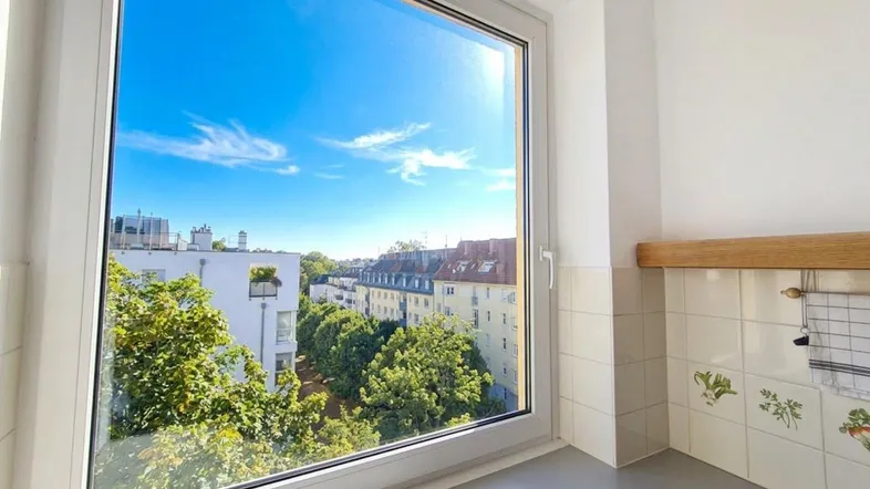 Heller Küchenbereich mit großem Fenster und Blick auf die umliegenden Gebäude und Bäume.