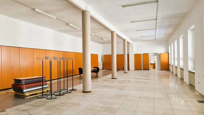 Großer, offener Büroraum mit vielen Fenstern, hohen Decken, Säulen und integrierten Holzschränken entlang der Wand.