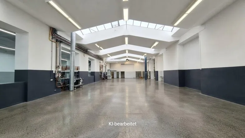 Große, leere Industriehalle mit hohen Decken, Betonboden und Oberlichtern für viel Tageslicht.