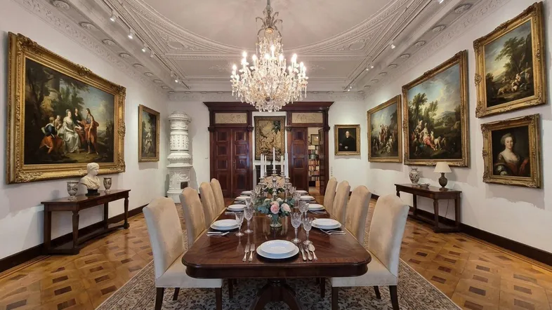 Elegantes Speisezimmer mit opulentem Kronleuchter, Stuckdecke und zahlreichen Gemälden, das eine aristokratische Atmosphäre schafft.