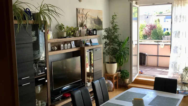 Heller Wohn- und Essbereich mit Holzboden, TV-Möbeln und Zugang zu einem Balkon.