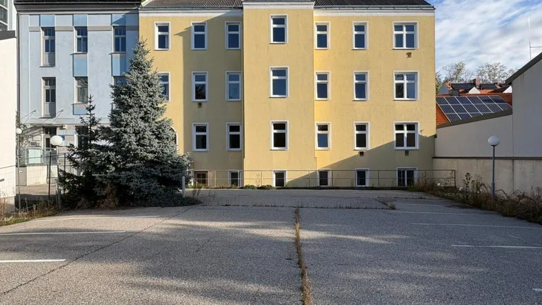Rückansicht eines Mehrfamilienhauses mit Parkplatz und Solaranlage auf dem Nachbardach.