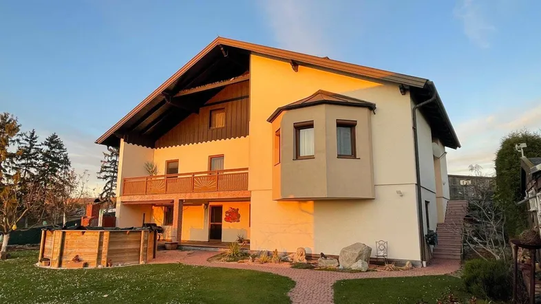 Rückansicht des Hauses mit Balkon, Erker und Gartenbereich im warmen Abendlicht.