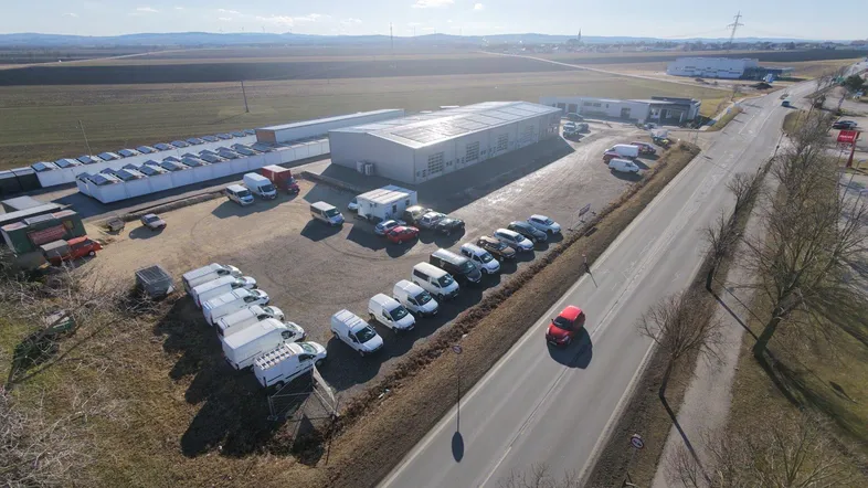 Luftaufnahme eines Gewerbegebäudes mit Photovoltaikanlage, umgeben von Feldern und einer Zufahrtsstraße.