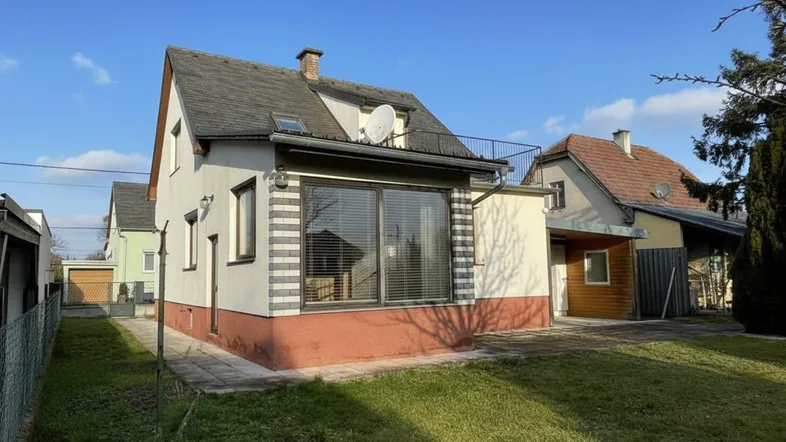 Freistehendes Haus mit Garten, großen Fenstern und einer kleinen Terrasse im Obergeschoss.