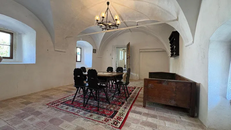 Historischer Essbereich mit Gewölbedecke, Terrakottaboden und rustikalen Holzmöbeln, beleuchtet von einem Kronleuchter.