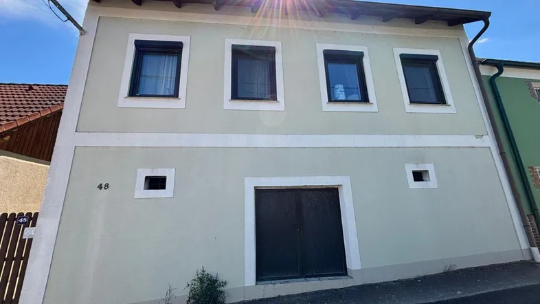 Fassade eines traditionellen Wohnhauses mit mehreren Fenstern und Rollläden unter blauem Himmel.