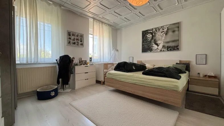 Schlafzimmer mit Doppelbett, hellem Laminatboden und dekorativer Deckenverkleidung.