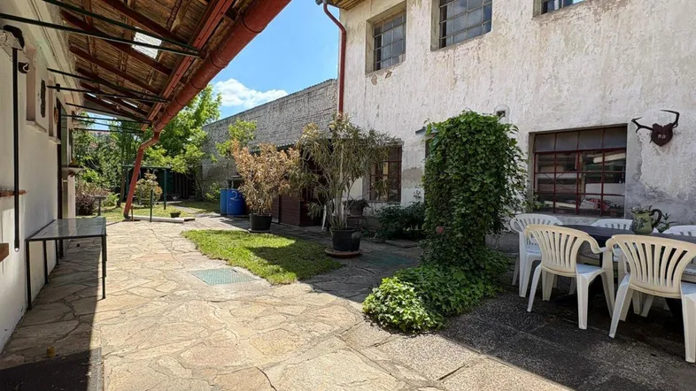Große gepflasterte Terrasse mit Gartenmöbeln und Blick auf das Gebäude unter blauem Himmel.