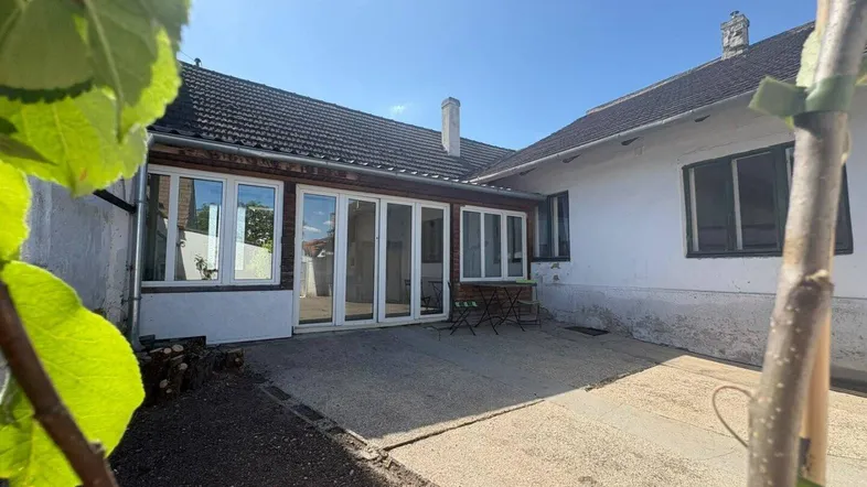 Sonniger Hinterhof mit gepflasterter Terrasse und großen Glasfronten zum Haus.