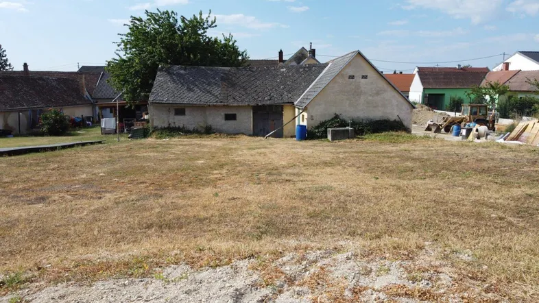 Blick auf ein trockenes Grundstück mit älteren Nebengebäuden und umliegenden Häusern in ländlicher Umgebung.