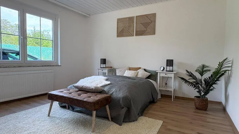 Helles Schlafzimmer mit Doppelbett, Nachttischen, großem Fenster und Holzdielen an der Decke.