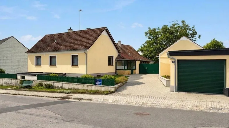Gelbes Einfamilienhaus mit braunem Ziegeldach, Vorgarten und separater Garage.