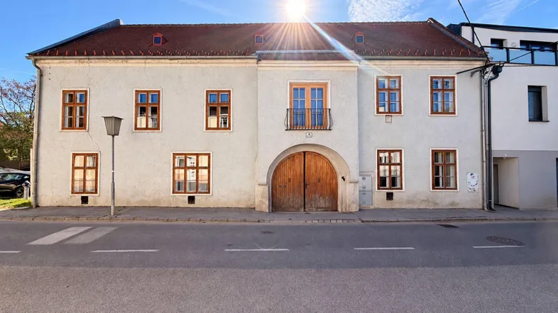 Historisches Gebäude mit heller Fassade, Holztüren und Fenstern, direkt an der Straße gelegen.