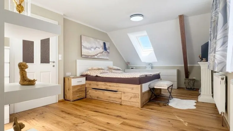 Helles Schlafzimmer im Dachgeschoss mit Holzboden, Dachfenster und modernem Bett mit Stauraum.