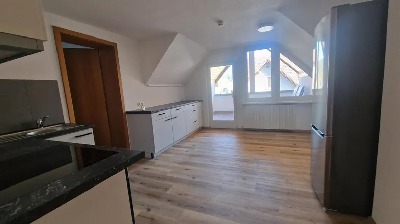 Helle Küche im Dachgeschoss mit modernen Unterschränken, Arbeitsplatte und Zugang zum Balkon.