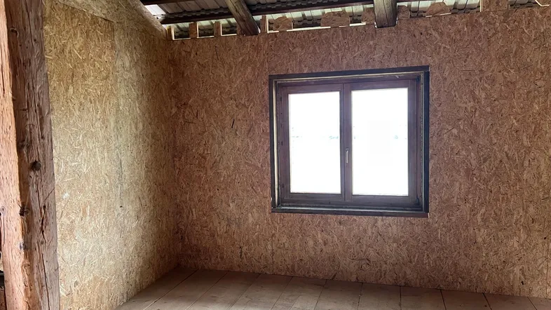 Unfertiger Dachbodenraum mit OSB-Plattenwänden, Holzboden und sichtbaren Dachbalken, bereit für den Ausbau.