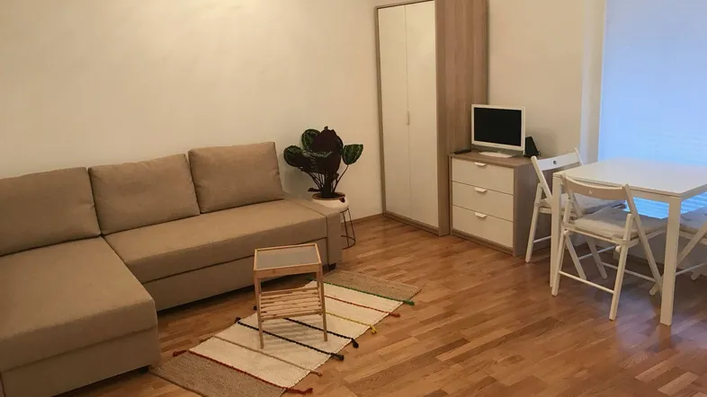 Heller Wohn- und Essbereich mit beigem Ecksofa, Esstisch und Holzfußboden.