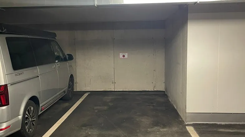 Leerer Stellplatz in einer Tiefgarage mit Betonwänden und Decke, beleuchtet von Leuchtstoffröhren.
