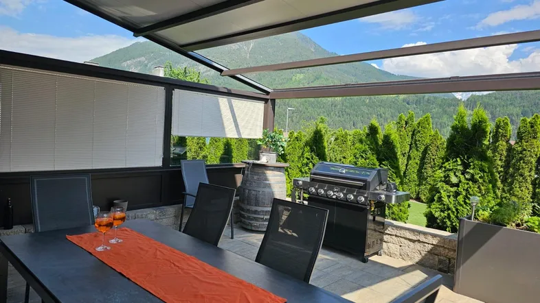 Geräumige Terrasse mit Esstisch, Grillbereich und schöner Aussicht auf die Berge.