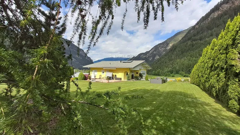 Weitläufiger Gartenbereich mit gepflegtem Rasen und einem charmanten Haus, umgeben von Bergen.