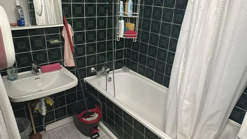 Badezimmer mit Badewanne, Duschvorhang und Waschbecken, gefliest in dunklem Grün und hellem Grau.