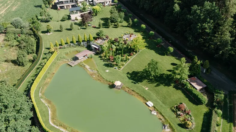 Luftaufnahme des weitläufigen Anwesens mit großem Teich, umgeben von grünen Feldern und Wald.