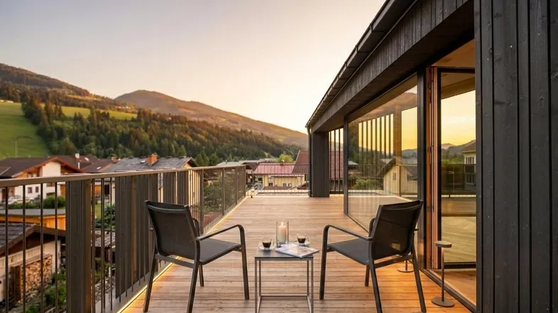 Geräumiger Balkon mit Holzboden, Sitzgelegenheiten und malerischem Bergblick bei Sonnenuntergang.
