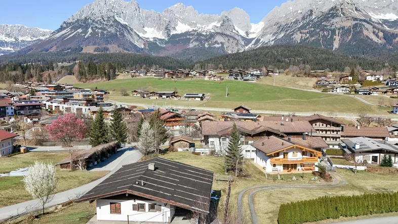 Luftaufnahme eines Hauses in einer malerischen Berglandschaft mit schneebedeckten Gipfeln im Hintergrund.
