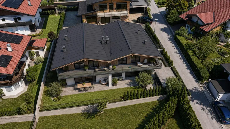 Luftaufnahme eines modernen Hauses mit dunklem Dach und gepflegtem Gartenbereich in einer Wohnsiedlung.