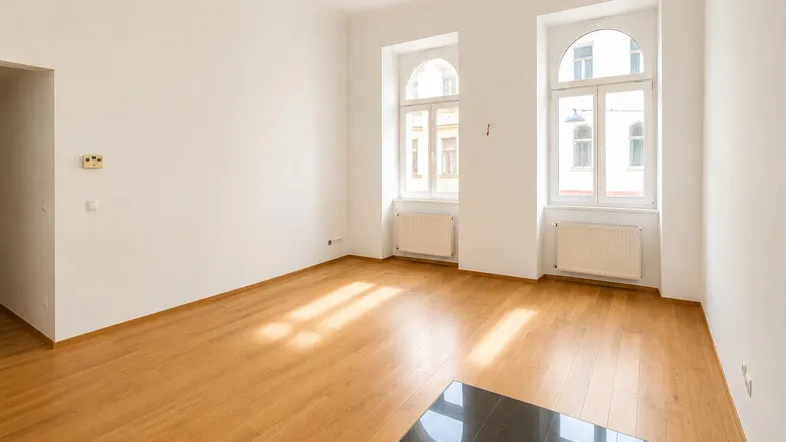 Helles, leeres Zimmer mit Holzboden und zwei hohen Rundbogenfenstern, ideal als Wohn- oder Schlafzimmer.