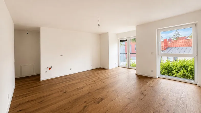 Helles, unmöbliertes Wohnzimmer mit neuem Holzboden und großen Fenstern, die viel Tageslicht hereinlassen.