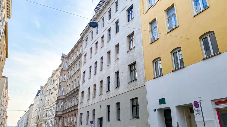 Blick auf die Straße mit mehreren Wohngebäuden und geparkten Autos unter blauem Himmel.