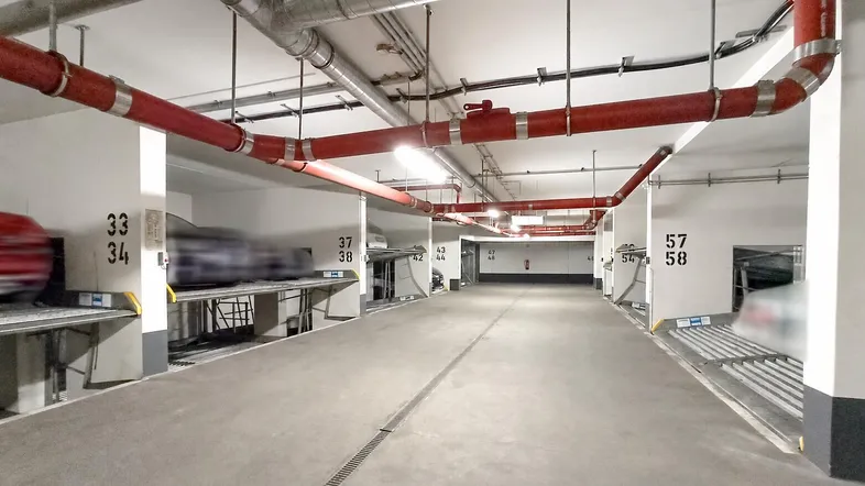 Geräumige Tiefgarage mit nummerierten Stellplätzen und sichtbaren roten Lüftungsrohren an der Decke.