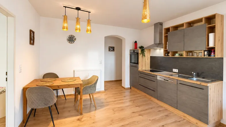 Moderne Küche mit grauen Fronten, Holzelementen, integrierten Geräten und Essbereich.