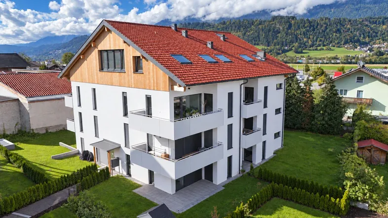 Neubau-Mehrfamilienhaus mit moderner Architektur, Balkonen und rotem Ziegeldach in grüner Umgebung.