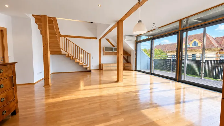 Helles und geräumiges Wohnzimmer mit Holzbalken, Parkettboden und Zugang zu einem großen Balkon.