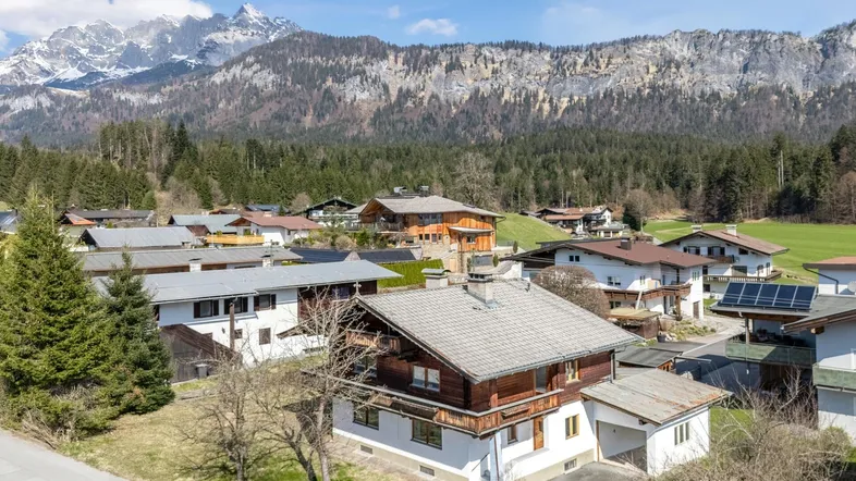 Blick über eine malerische Wohnsiedlung mit traditionellen Häusern vor einer beeindruckenden Bergkulisse.