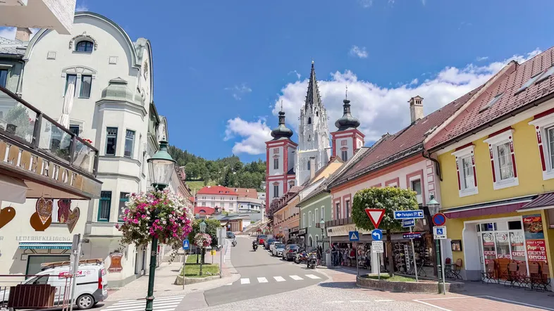 Belebte Straße in einer historischen Stadt mit traditionellen Gebäuden und einer markanten Kirche im Hintergrund.