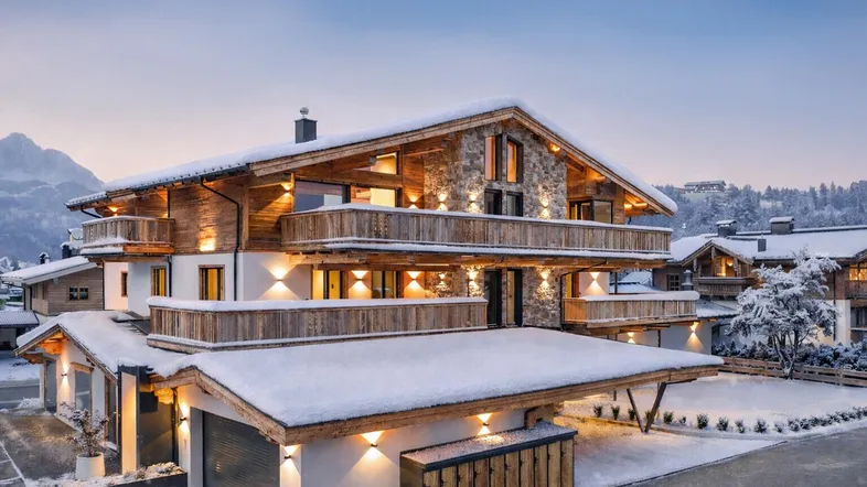 Luxuriöses Chalet im alpinen Stil mit mehreren Balkonen und verschneiter Umgebung bei Sonnenuntergang.
